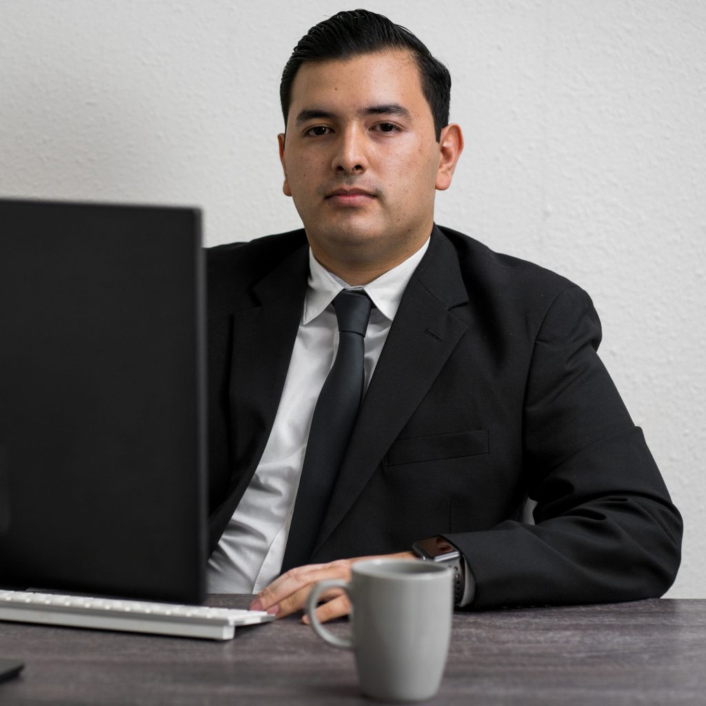 Male lawyer in black suit sitting in front of a laptop with a mug on the table.
