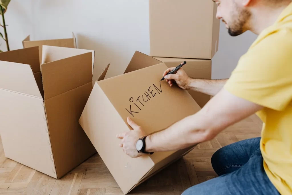 A man writing the word “kitchen” on a cardboard box.