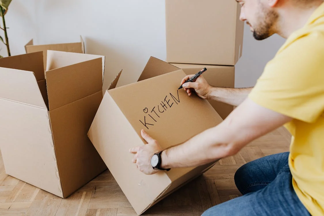 A man writing the word “kitchen” on a cardboard box.