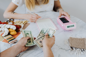 Female counting expenses on a table, with hands opposite her holding money in cash.
