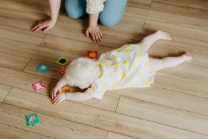 A baby girl is lying on the floor playing.