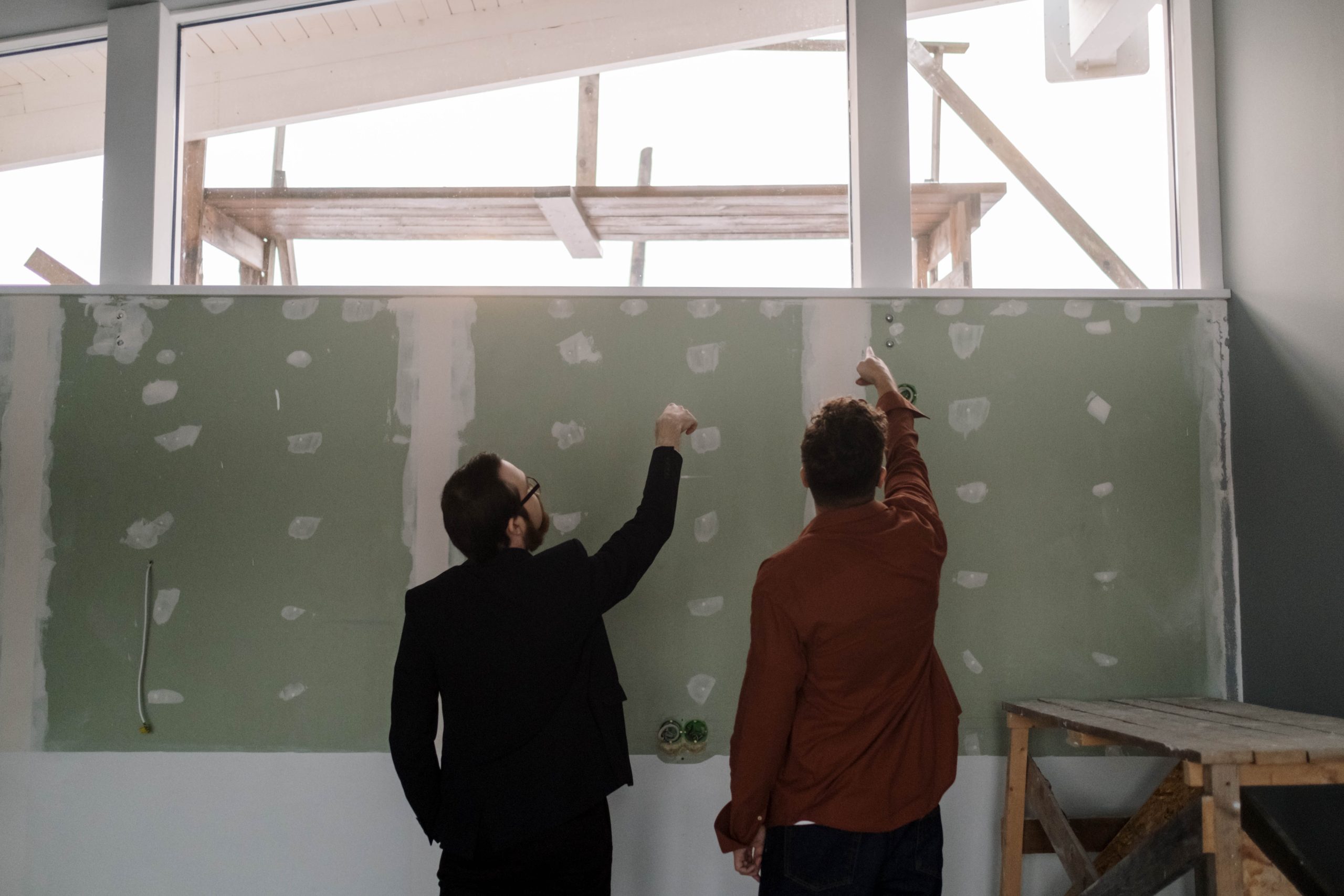 Two men pointing at the unfinished wall. Common Drywall Repair Issues