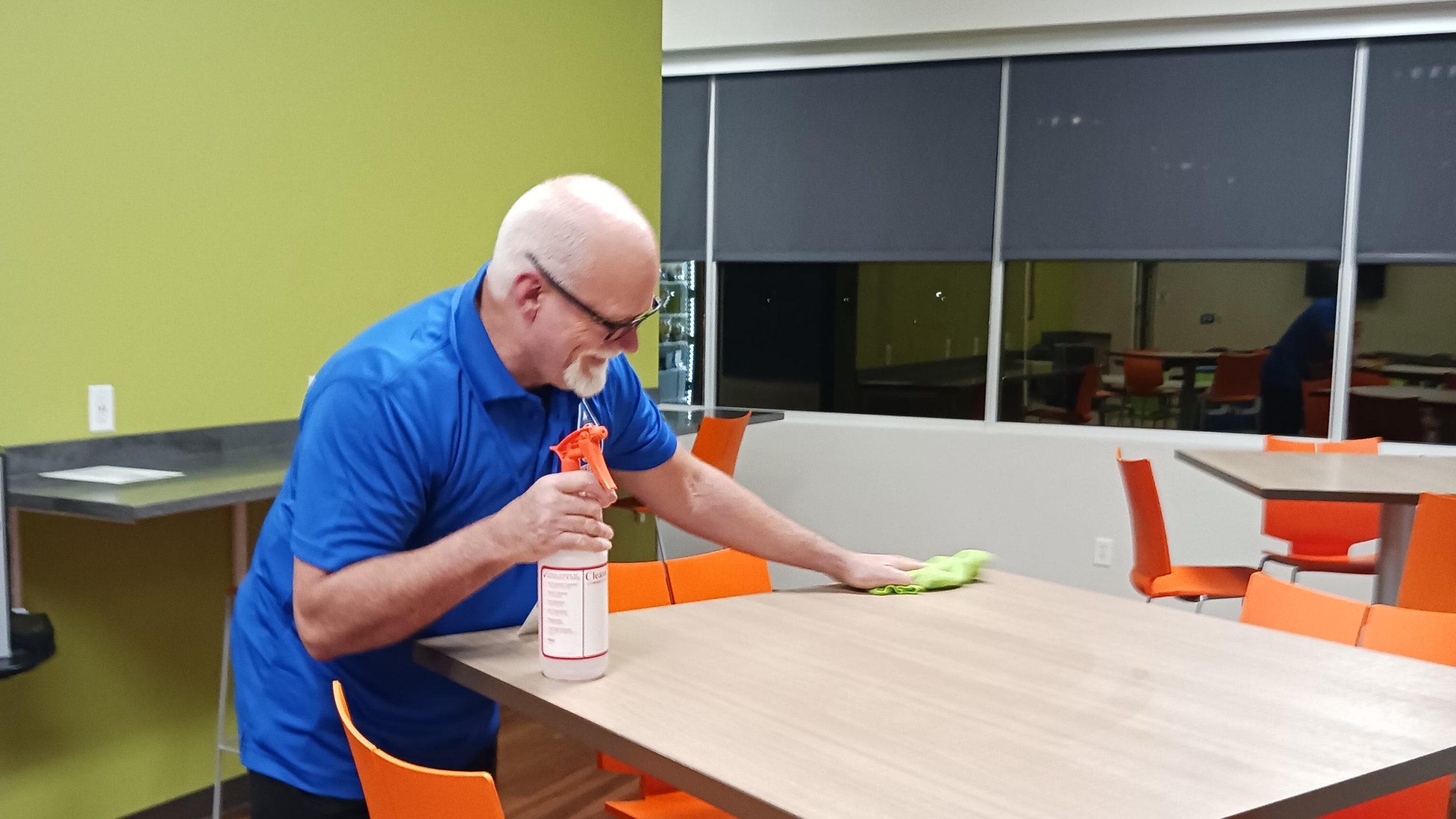 A man from a commercial sanitation service wiping off the surface of a table.